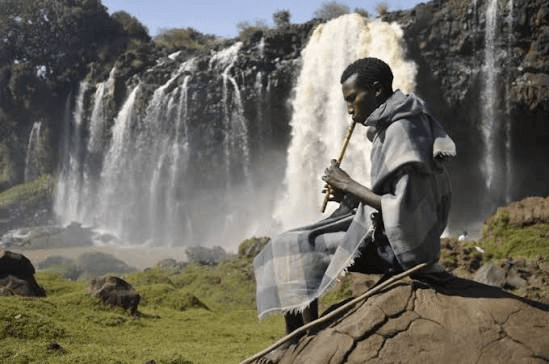 A man playing a washint flute beside the Blue Nile Falls